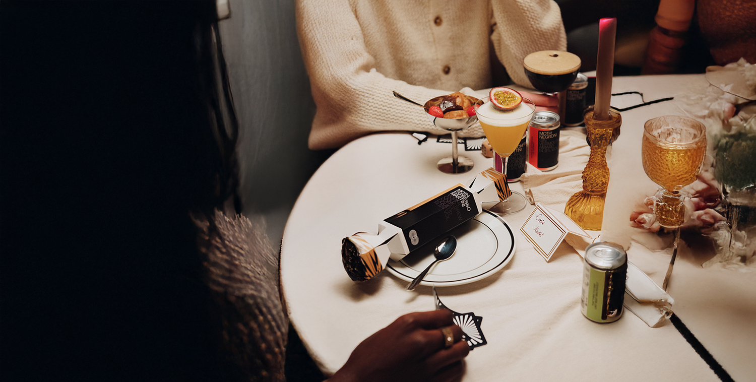 Person sitting at a table with drinks and snacks, possibly in a cafe or restaurant.